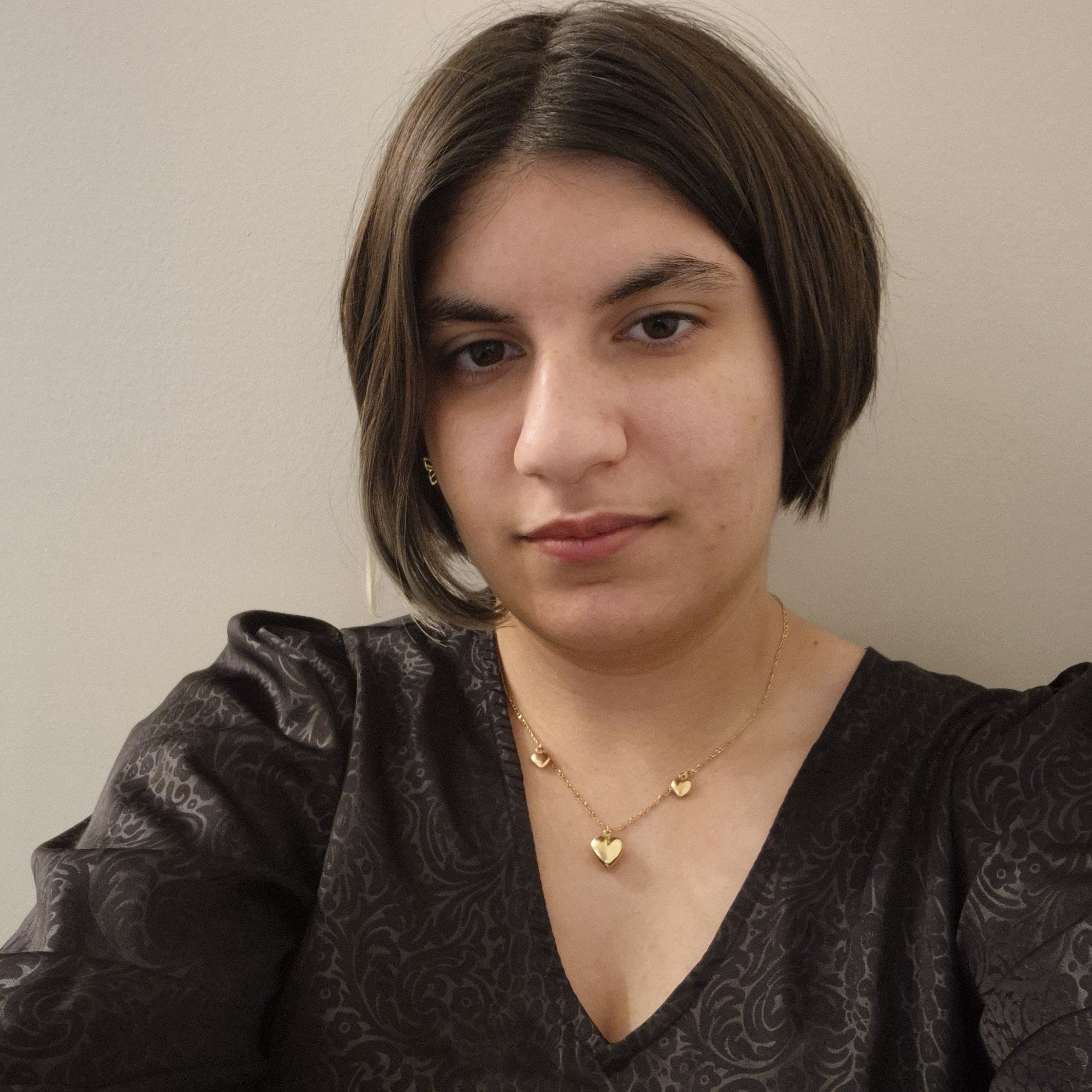 Photograph of 'Yasemin Gunal', short brown hair, light skin, wearing a patterend black shirt and gold coloured jewlery